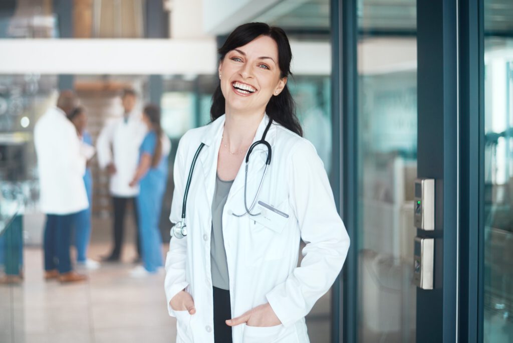 Portraet einer selbstbewussten Aerztin die in einem Krankenhaus arbeitet mit ihren Kollegen im Hintergrund